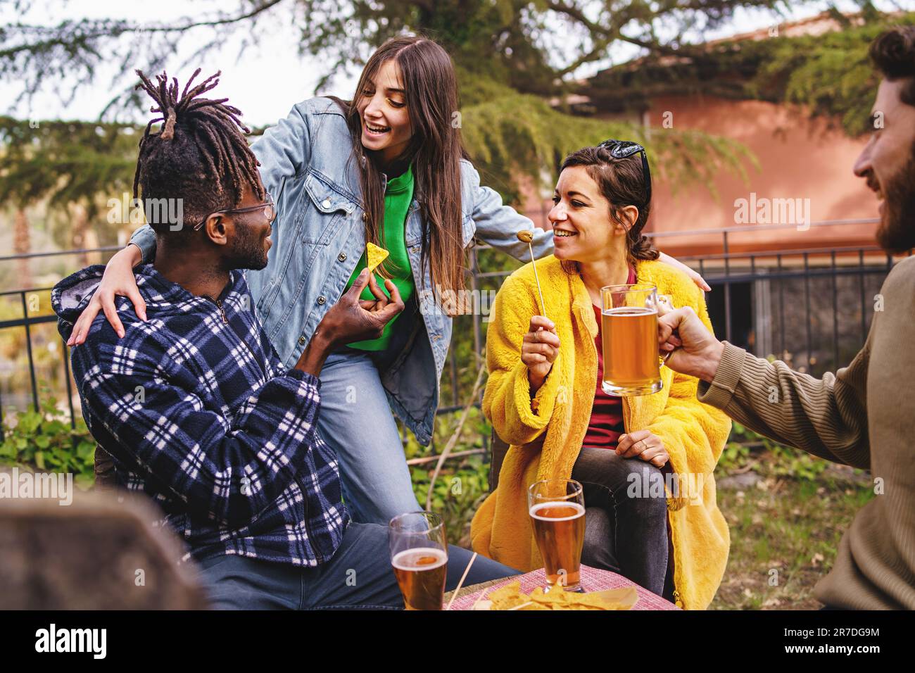 Eine vielfältige Gruppe von Freunden begrüßt Sie in einem Biergarten im Freien, wo Sie Bier, Nachos und Olivenvorspeisen genießen. Stockfoto