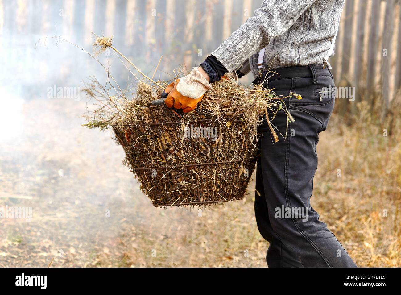 Arbeiten Sie im Freien im Garten. Ein Mensch hält einen Korb mit trockenem Gras. Entfernen Sie