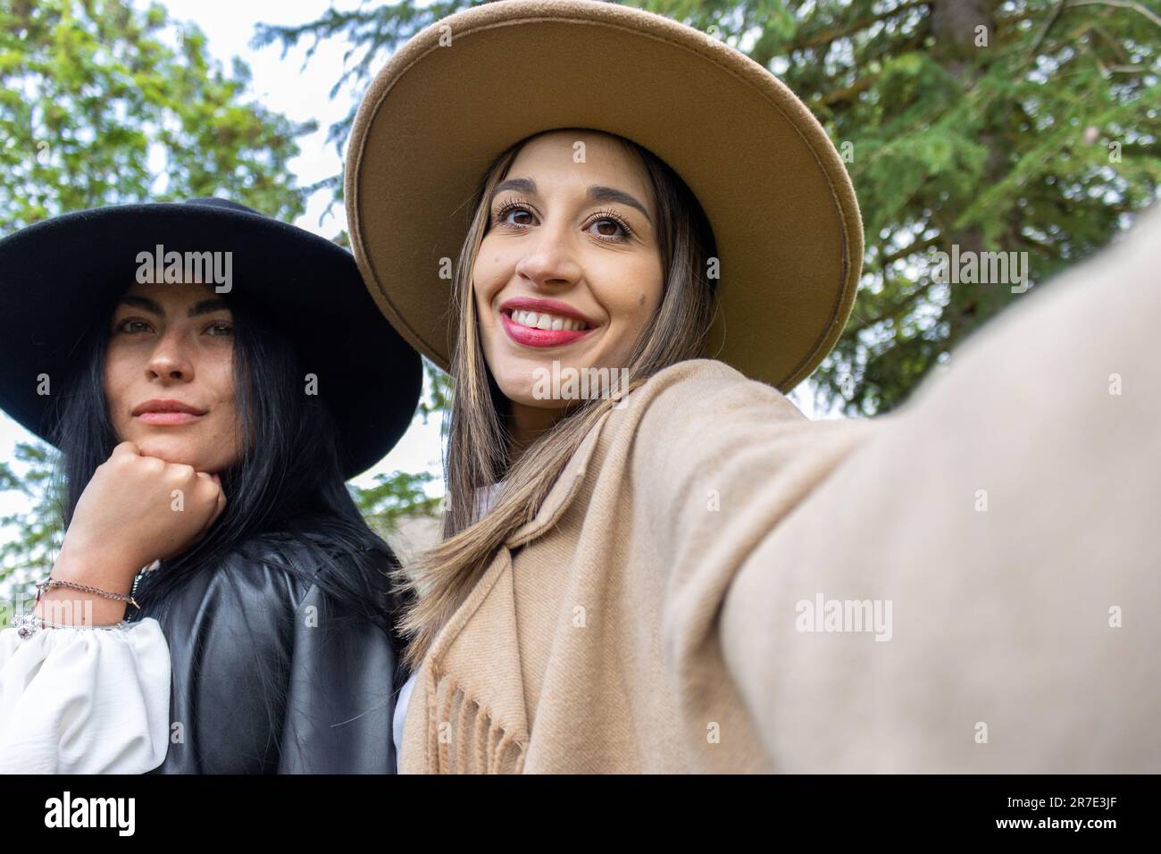 Zwei stylische junge Frauen in modischen Hüten machen ein Selfie, während sie in einem Park stehen Stockfoto