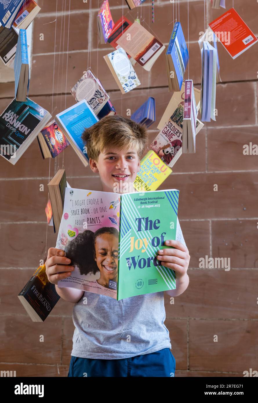 Ein 12-jähriger Junge liest das Programm des Edinburgh International Book Festival 2023, umgeben von Taschenbüchern zur Programmeinführung, Schottland, Großbritannien Stockfoto