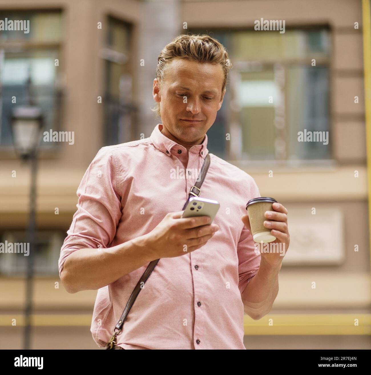 Ein Mann mittleren Alters, der am Telefon SMS schreibt. Er genießt eine Tasse Kaffee aus Pappbechern auf der Straße der Sommerstadt. Schnittpunkt der Technologie, während der Mensch in der mobilen Kommunikation während einer Kaffeepause ist. . Hochwertiges Foto Stockfoto