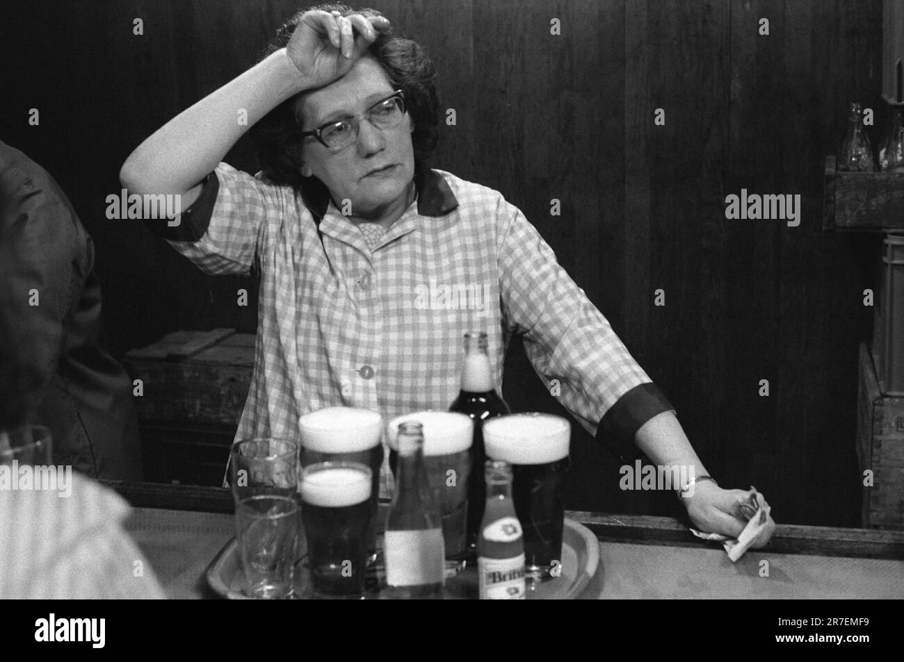 Das Barpersonal, eine Barkeeper, die einen typischen Hauskittel trägt, über ihren Alltagskleidung, sie ist erschöpft, müde, dies ist ein Teilzeitjob am Abend. Byker and St Peters Working Men's Club, Newcastle upon Tyne, Tyne and Wear, Nordengland um 1973. 1970S UK HOMER SYKES Stockfoto
