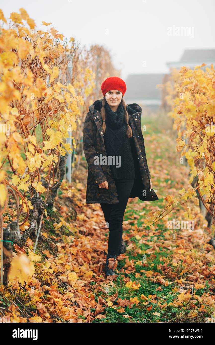 Junge Frau, die im Herbst in den Weinbergen von Lavaux wandert und eine warme Militärjacke und rote Baskenmütze trägt Stockfoto