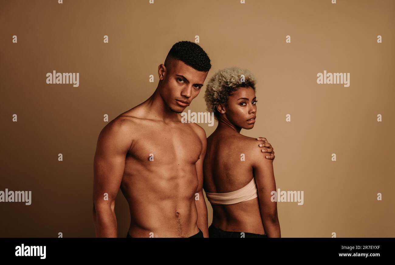 Ein junges afrikanisches Paar steht selbstbewusst in einem Studio zusammen und zeigt seine Passform und seine Muskeln sowie seine melaninreiche Haut gegen ein m Stockfoto