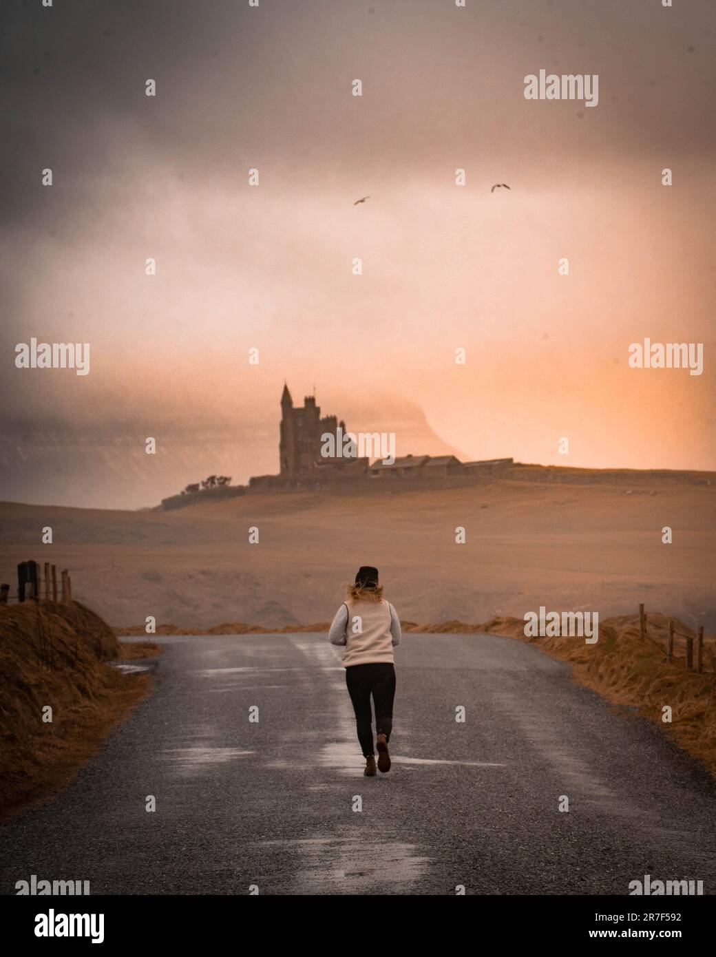 Eine junge Frau läuft auf einer einsamen Straße mit einem atemberaubenden Sonnenuntergang im Hintergrund Stockfoto
