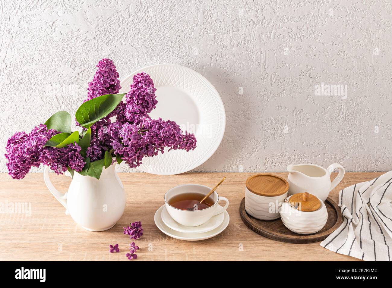 Eine große Tasse Tee auf der Küche mit Holzarbeitsfläche und Teeutensilien für Teetrinken. Blumenstrauß in einem weißen Krug. Küchenhintergrund Stockfoto