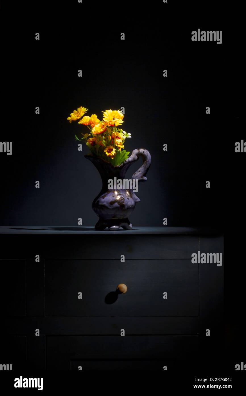 Stille Leben einer gelben Blume in einer Vase auf einem Sideboard. Blauer Hintergrund Stockfoto