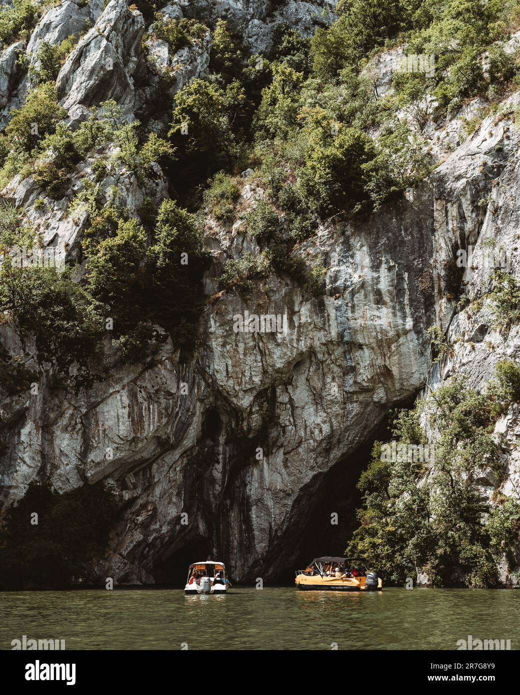 Eine vertikale Aufnahme von Booten, die in der Nähe einer großen Klippe auf der Donau segeln Stockfoto