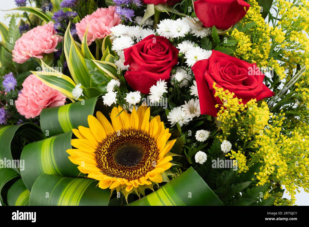 Farbenfroher Blumenstrauß mit Rosen und Sonnenblumen auf grünem Blatthintergrund Stockfoto
