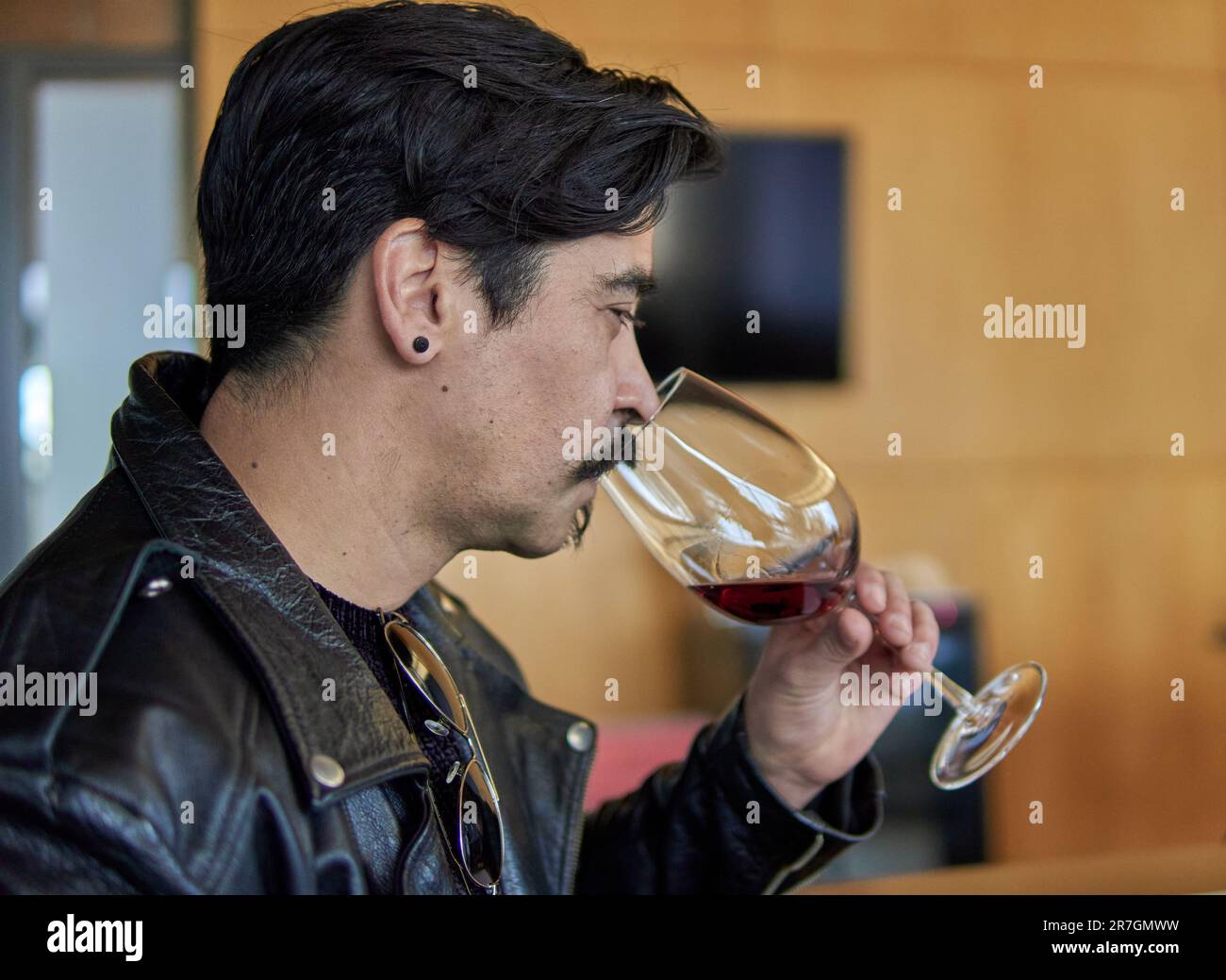 ein lateinischer Mann im Profil bei einer Weinprobe in einem Weinkeller in mendoza argentina. Brauner Mann in Lederjacke mit Schnurrbart, der sich hält und riecht Stockfoto