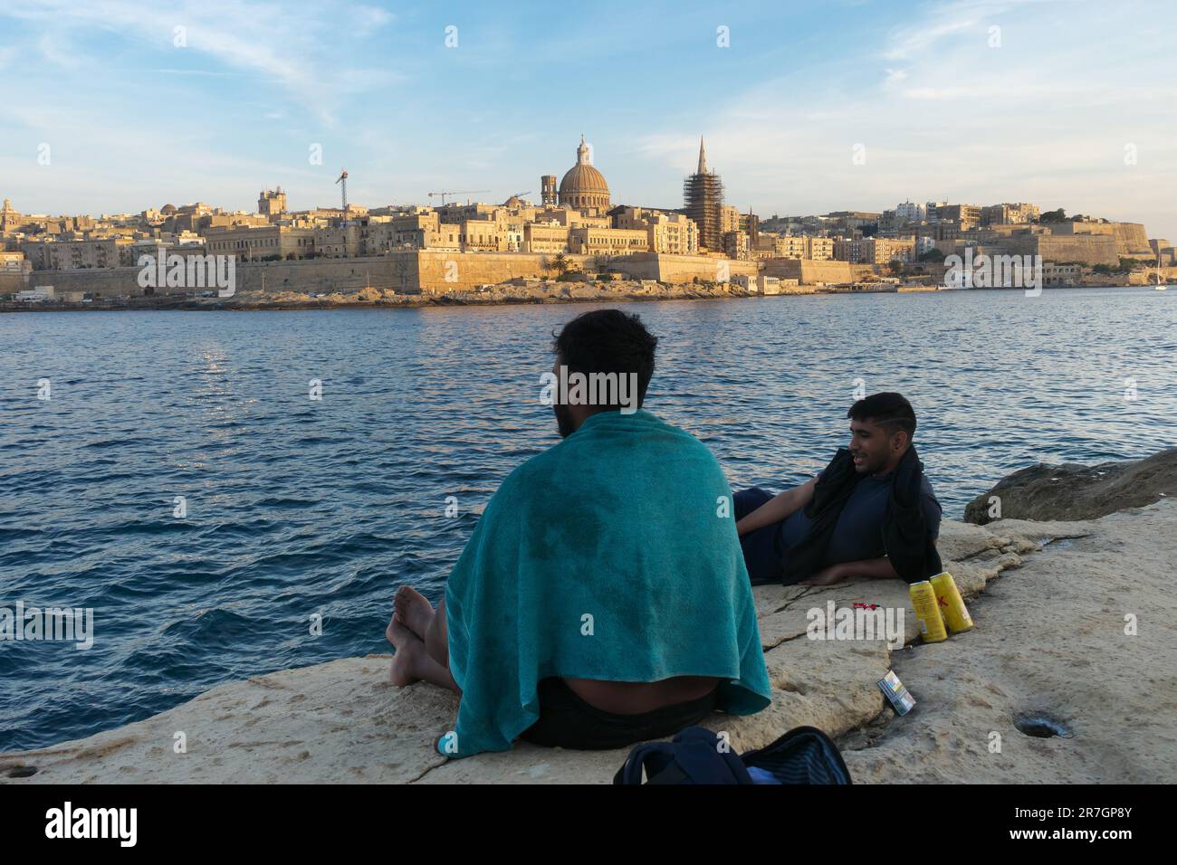 Sliema Felsenstrand, zwei Personen, die sich weit weg von der Stadt Valletta bei Sonnenuntergang, Malta, entspannen Stockfoto