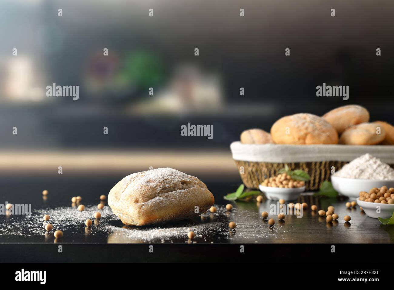 Sojamehlbrot und Getreide auf schwarzer Küchenbank und Korb voller Brot im Hintergrund. Vorderansicht. Stockfoto