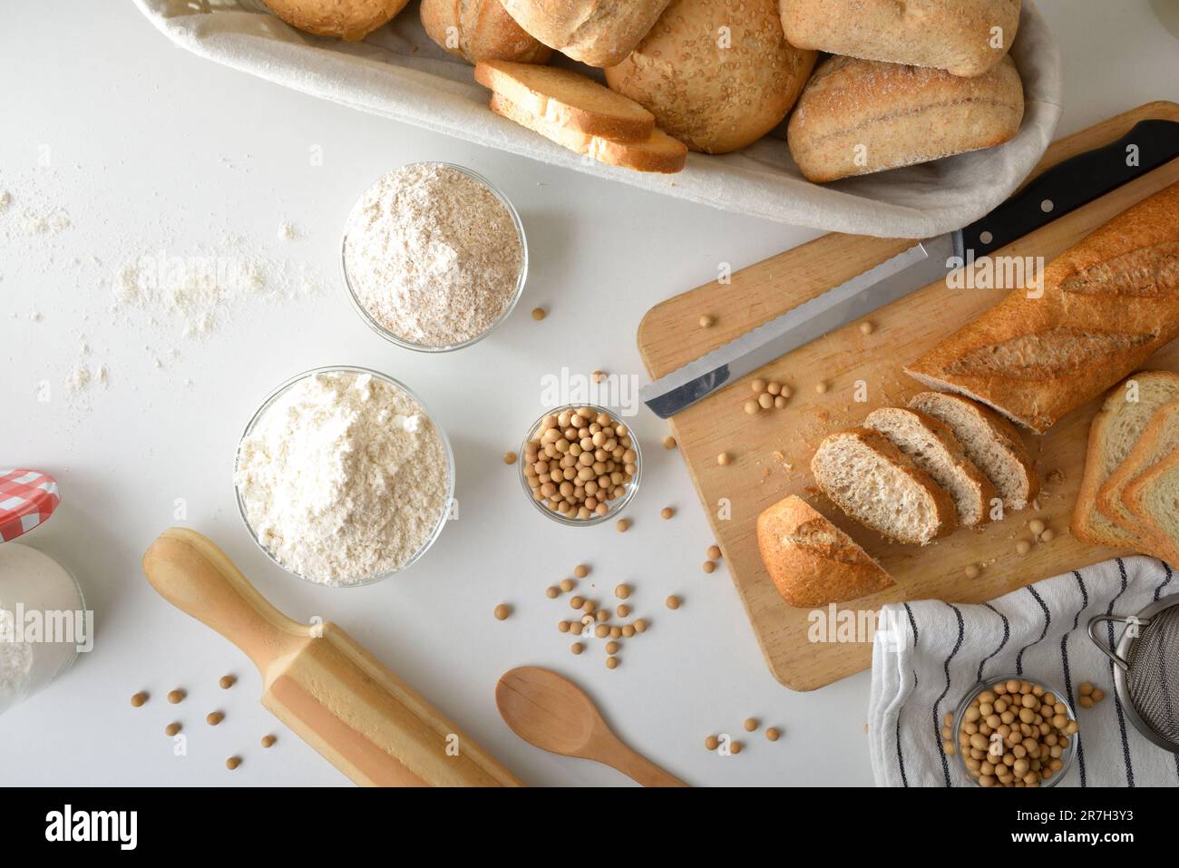 Frisches Brot mit Sojamehl auf weißem Tisch und Schneidebrett mit Scheiben. Draufsicht. Stockfoto