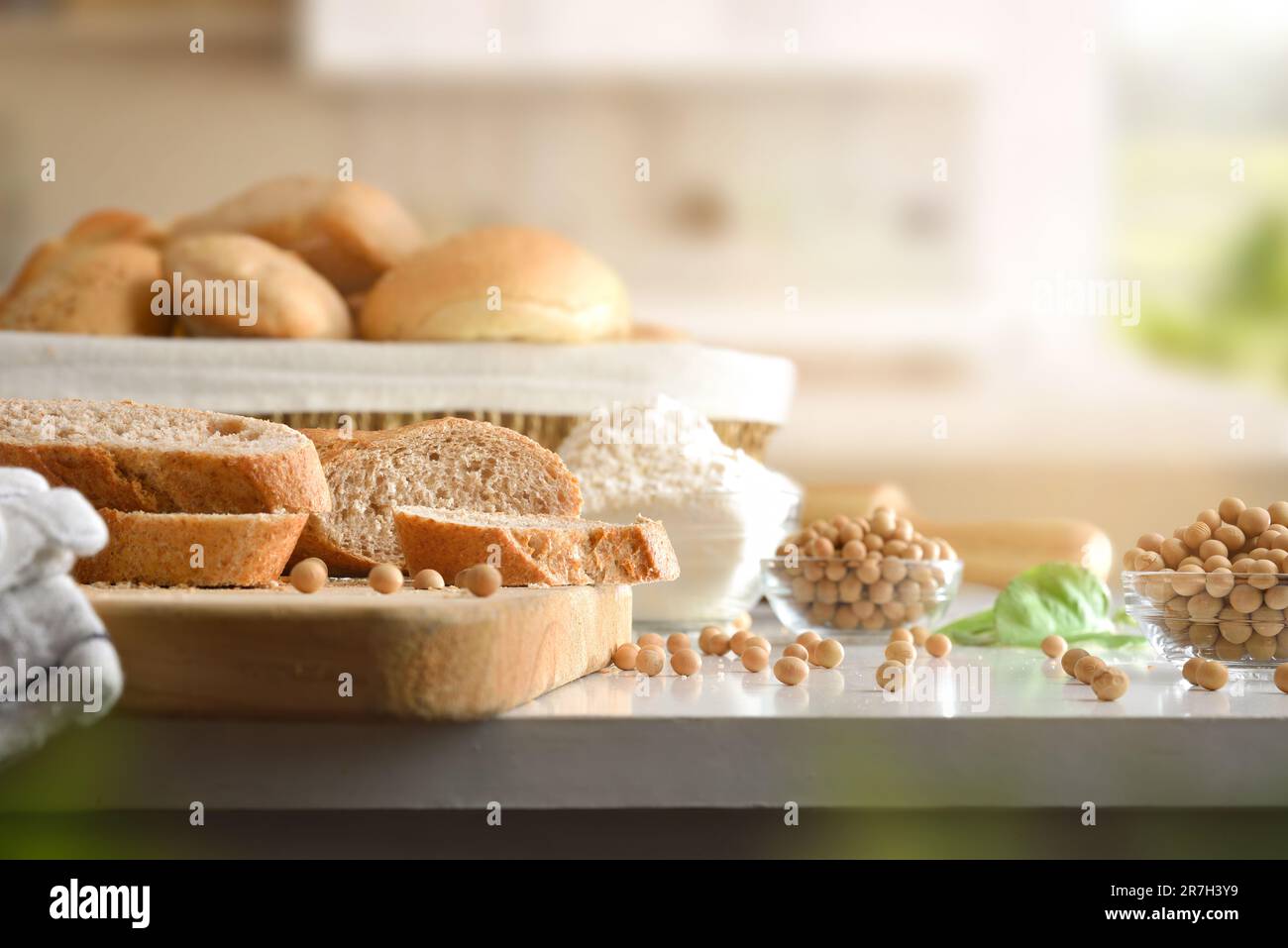 Scheiben und Brot mit Sojamehl auf dem Schneidebrett und im Korb auf der weißen Küchenbank. Vorderansicht. Stockfoto