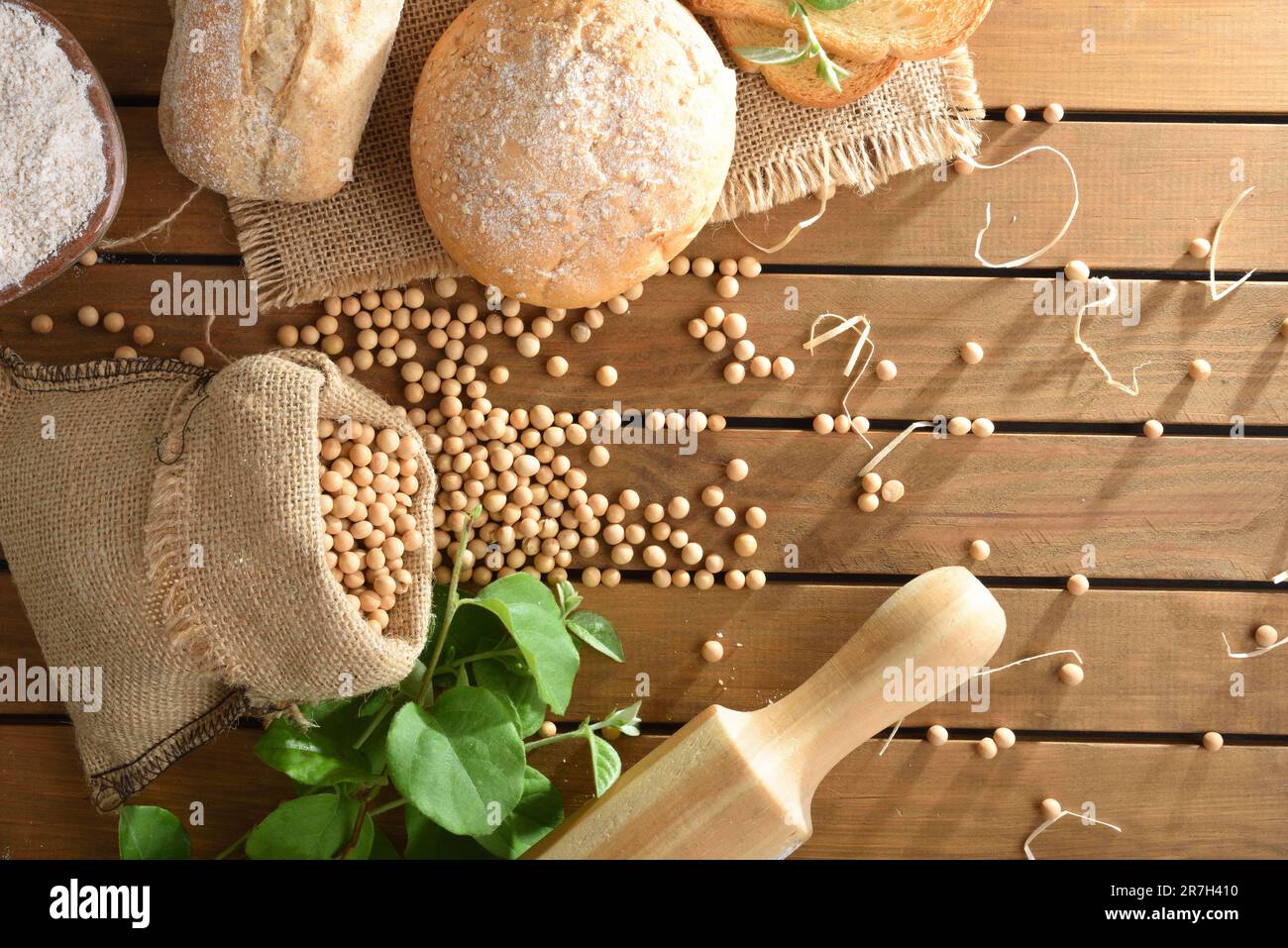 Sojamehlbrot auf einem Holztisch mit einem Sack voller Sojabohnen, Mehl, Brötchen und Blättern. Draufsicht. Stockfoto