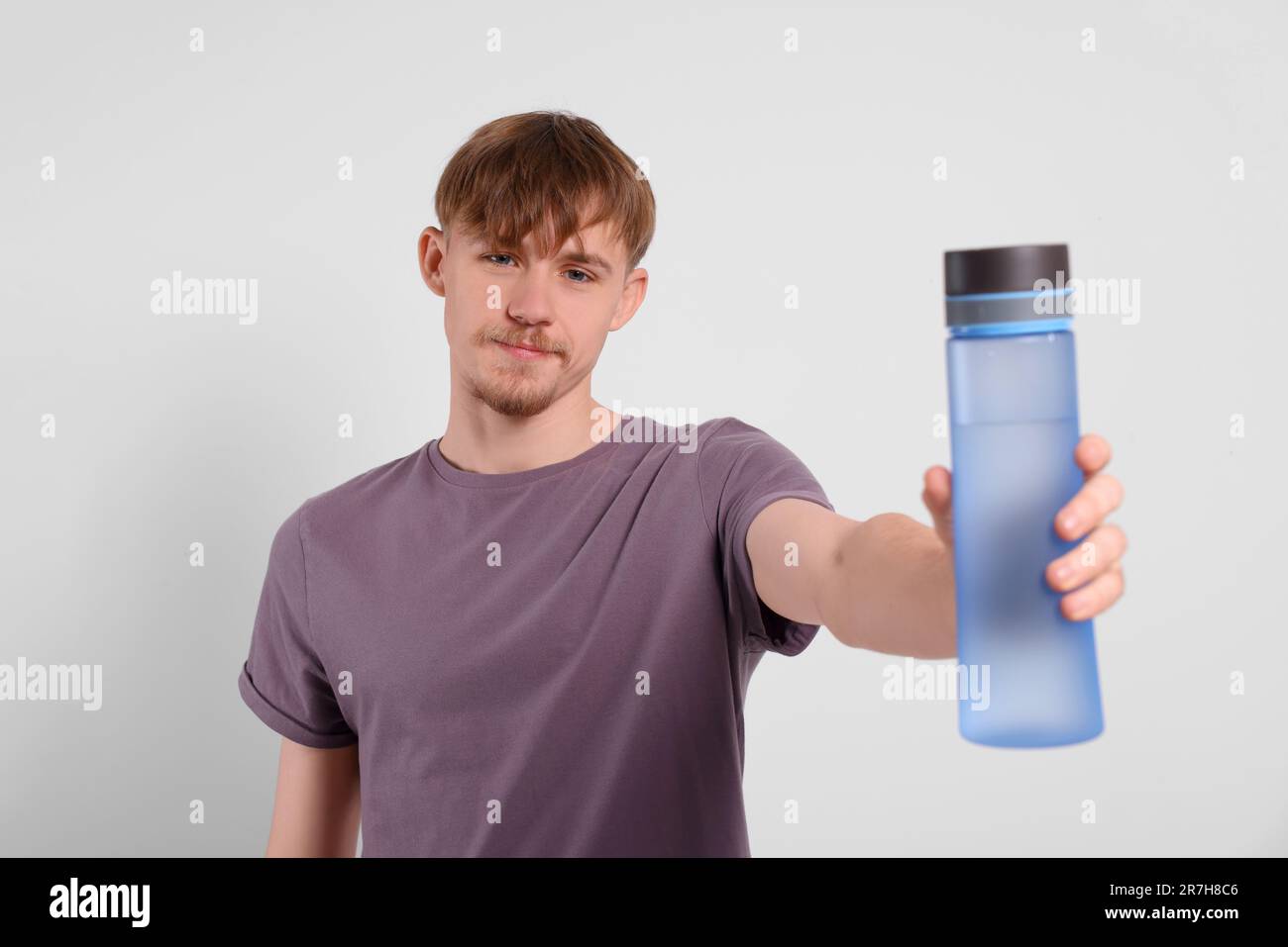 Mann mit transparenter Kunststoffflasche und Getränk auf hellgrauem Hintergrund Stockfoto