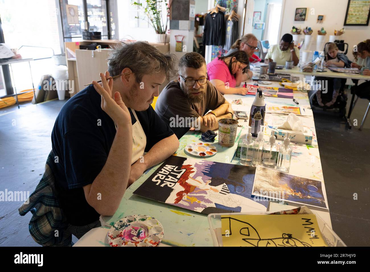 Asheville, North Carolina, USA. 9. Juni 2023. Ein junger Mann mit Entwicklungsbehinderung arbeitet an einem Malprojekt mit einem Kunstlehrer, der auch als direkter Unterstützer im Open Hearts Art Center arbeitet, einem gemeinnützigen Studio und einer Galerie, die auch als Tageszentrum fungieren. Das Zentrum repräsentiert und befähigt Erwachsene mit unterschiedlichen Behinderungen, ihr volles Potenzial durch die Kunst zu entfalten. (Kreditbild: © Robin Rayne/ZUMA Press Wire) NUR REDAKTIONELLE VERWENDUNG! Nicht für den kommerziellen GEBRAUCH! Stockfoto