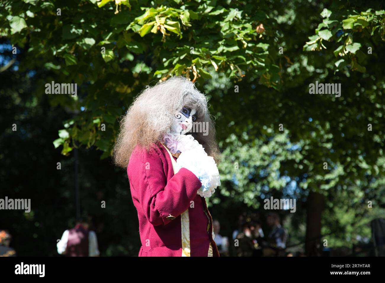 Ein reifer weißer Mann mit langen weißen Haaren, einem leuchtend roten Kostüm und einem Kopfschmuck mit Fell und Perücke, der zur Seite blickt Stockfoto