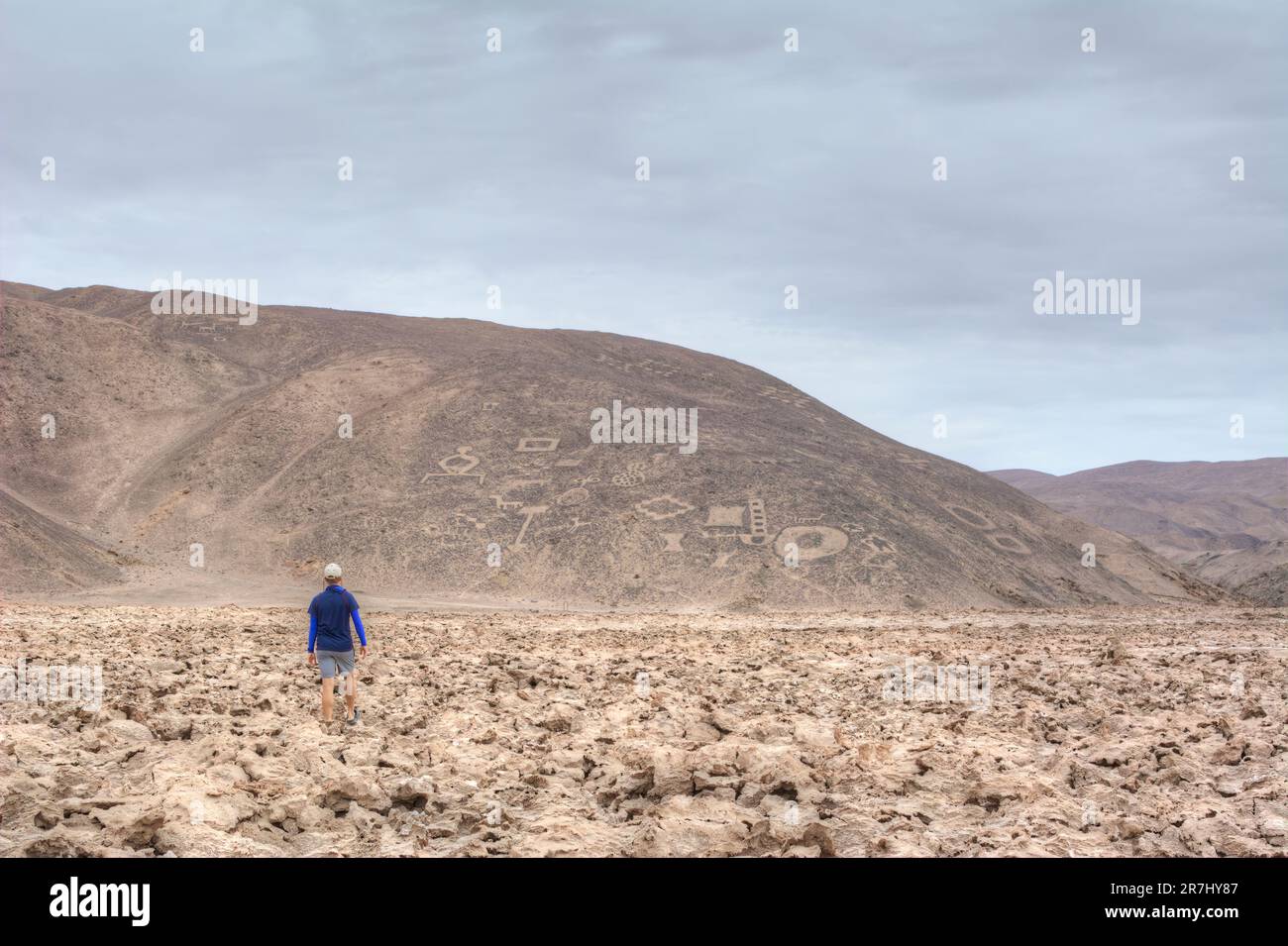 Ein Mann geht über die Ebene in Richtung der Hügel mit zahlreichen antiken Felszeichnungen (Geoglifos de Cerro Pintados) in Chile Stockfoto