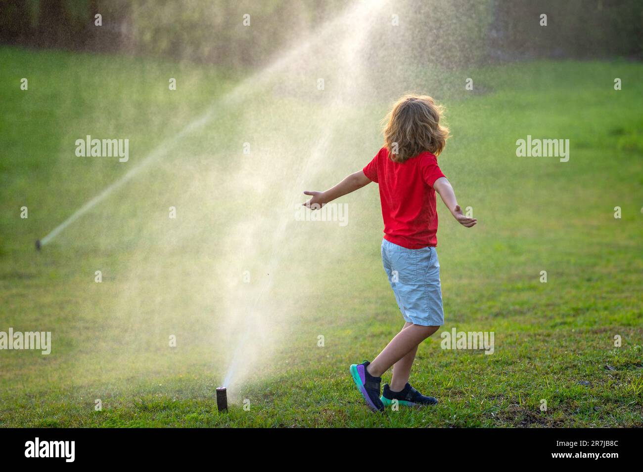 Süßes kleines Kind, das im Sommer Gras im Garten gießt. Kinderspiel im