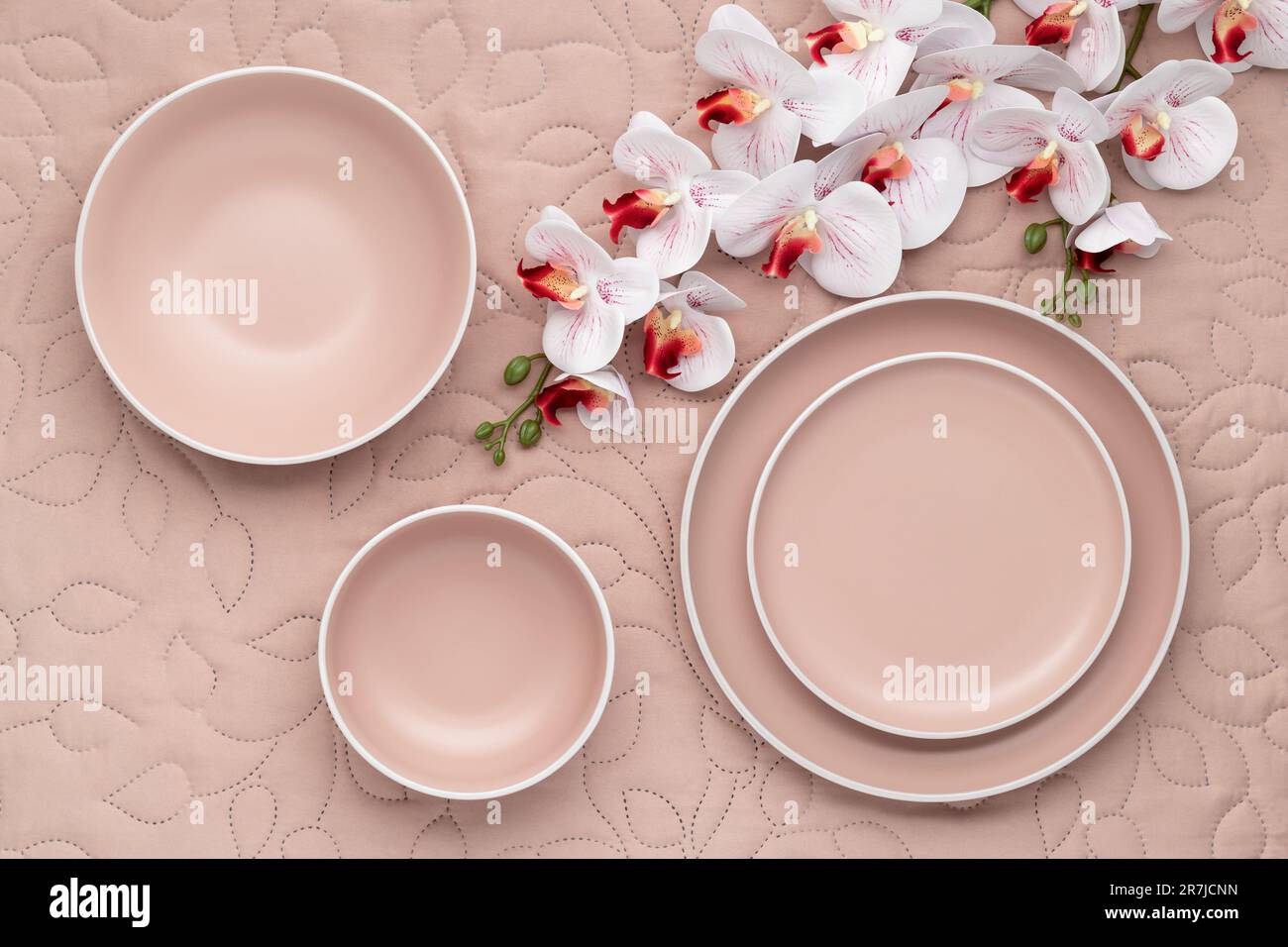 Ein Set cremefarbener Platten in verschiedenen Größen und Blumenstrauß auf dem Tisch, Draufsicht. Ein leeres Geschirr auf einer hellen beigen Tischdecke. Modernes t Stockfoto