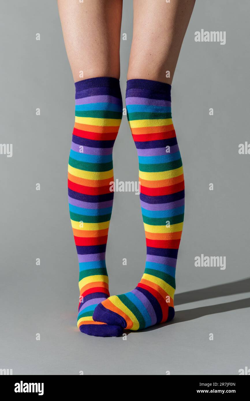 Zugeschnittene Beine einer nicht wiedererkennbaren Frau in gestreiften, bunten Socken, die im Studio vor grauem Hintergrund stehen und Schatten auf dem Boden haben Stockfoto