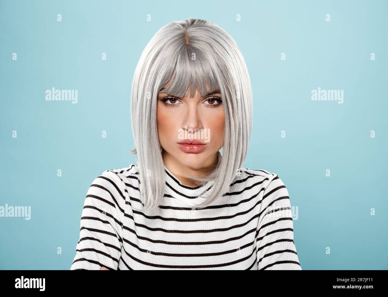 Ein junges Mädchen mit grauen Haaren im gestreiften T-Shirt, das vor blauem Hintergrund auf die Kamera schaut Stockfoto