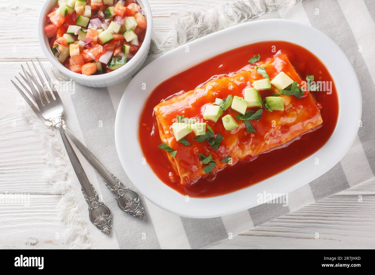 Nasse Burritos haben ein Hackfleisch und gekühlte Bohnenfüllung, verpackt in eine große Tortilla, erstickt mit roter Sauce und geschmolzenem Käse, auf dem Teller o Stockfoto