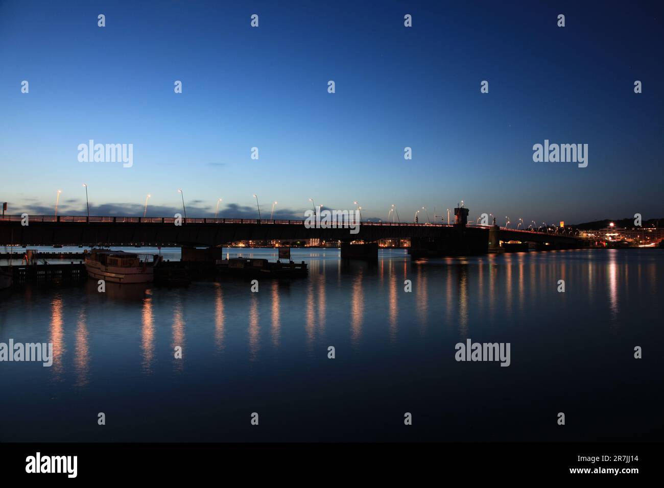 Eine große Brücke, beleuchtet durch künstliche Beleuchtung bei Nacht, die sich über ein breites Gewässer erstreckt Stockfoto