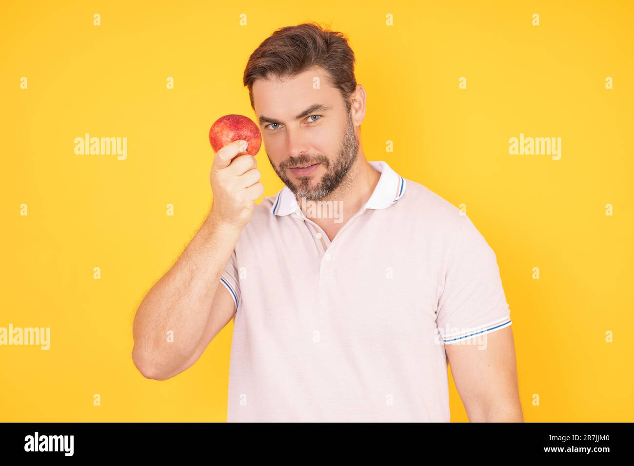 Stomatologisches Konzept. Ein Mann mit perfektem Lächeln, der Apfel auf einem gelben, isolierten Studio-Hintergrund hält. Mann isst grünen Apfel. Porträt des Mannes mittleren Alters mit Stockfoto