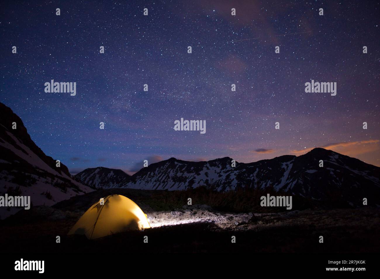 Die Milchstraße funkelt am Nachthimmel über einem beleuchteten Zelt und den Never Summer Mountains von Colorado. Stockfoto