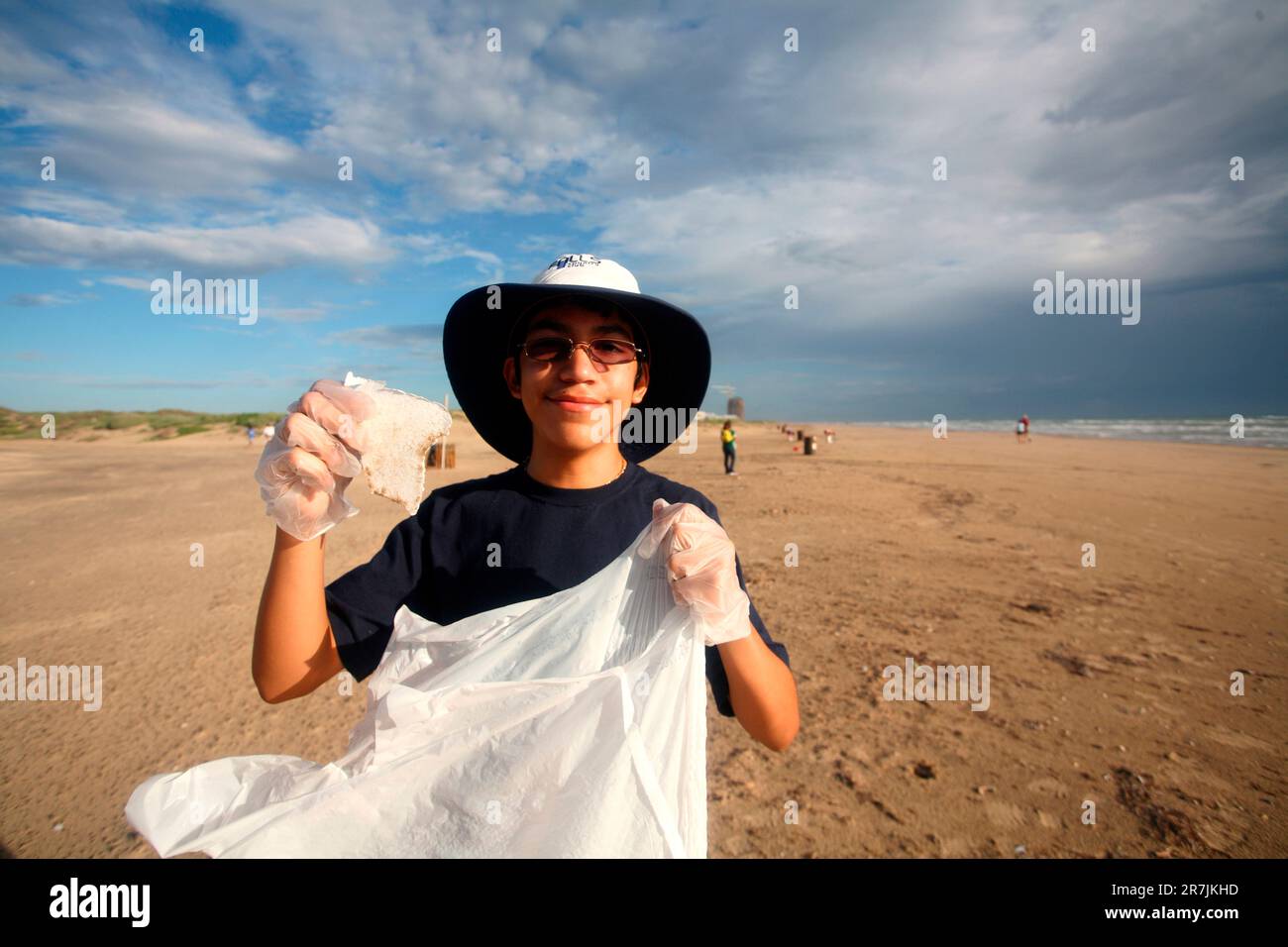 Ein kleiner Junge posiert für die Kamera, während er den Strand aufräumt. Stockfoto