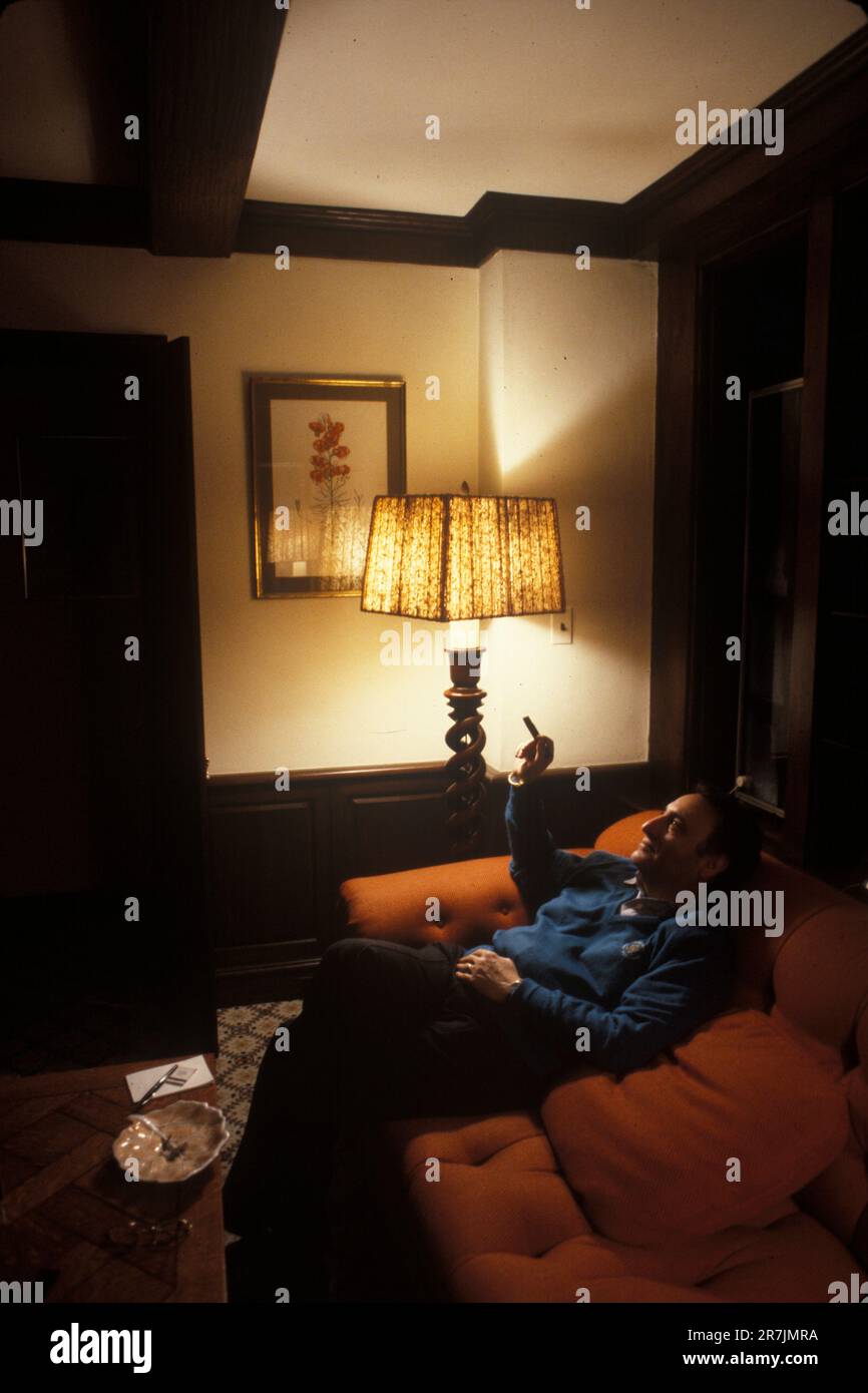 Der ehemalige Vorsitzende eines großen Finanzunternehmens entspannt sich mit einer Zigarre im schwach beleuchteten Wohnzimmer seines Hauses in Connecticut. Stockfoto