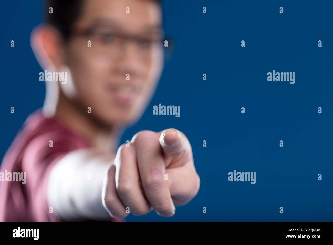 Fingerspitze auf einem transparenten Bildschirm mit scharfem Fokus, verschwommener asiatischer Mann mit Brille im Hintergrund auf Blau. Ideal für Touch-Grafikanwendungen Stockfoto