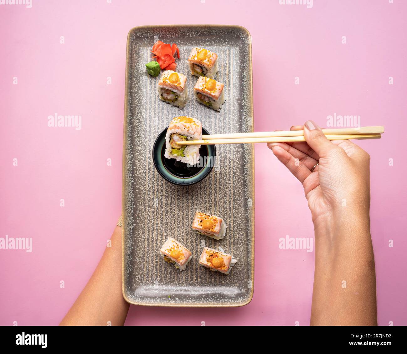 Ein Blick von oben auf eine elegante Platte mit Sushi-Rollen vor einem leuchtend rosa Hintergrund Stockfoto