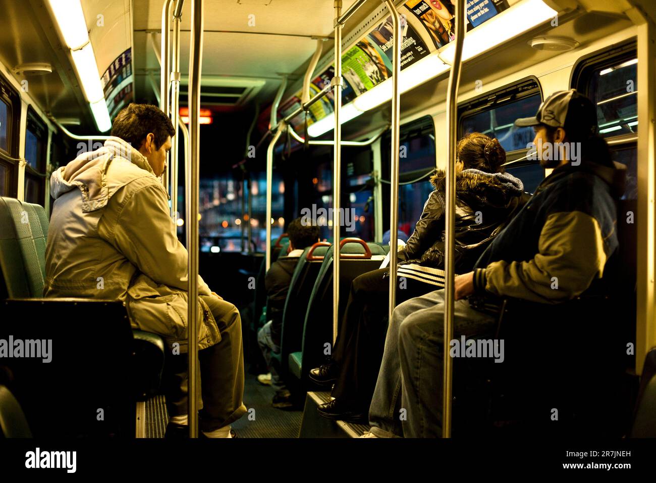 Mehrere Passagiere sitzen in einem Bus in Seattle, Washington, während der Bus in der Dämmerung durch den Verkehr fährt. Stockfoto