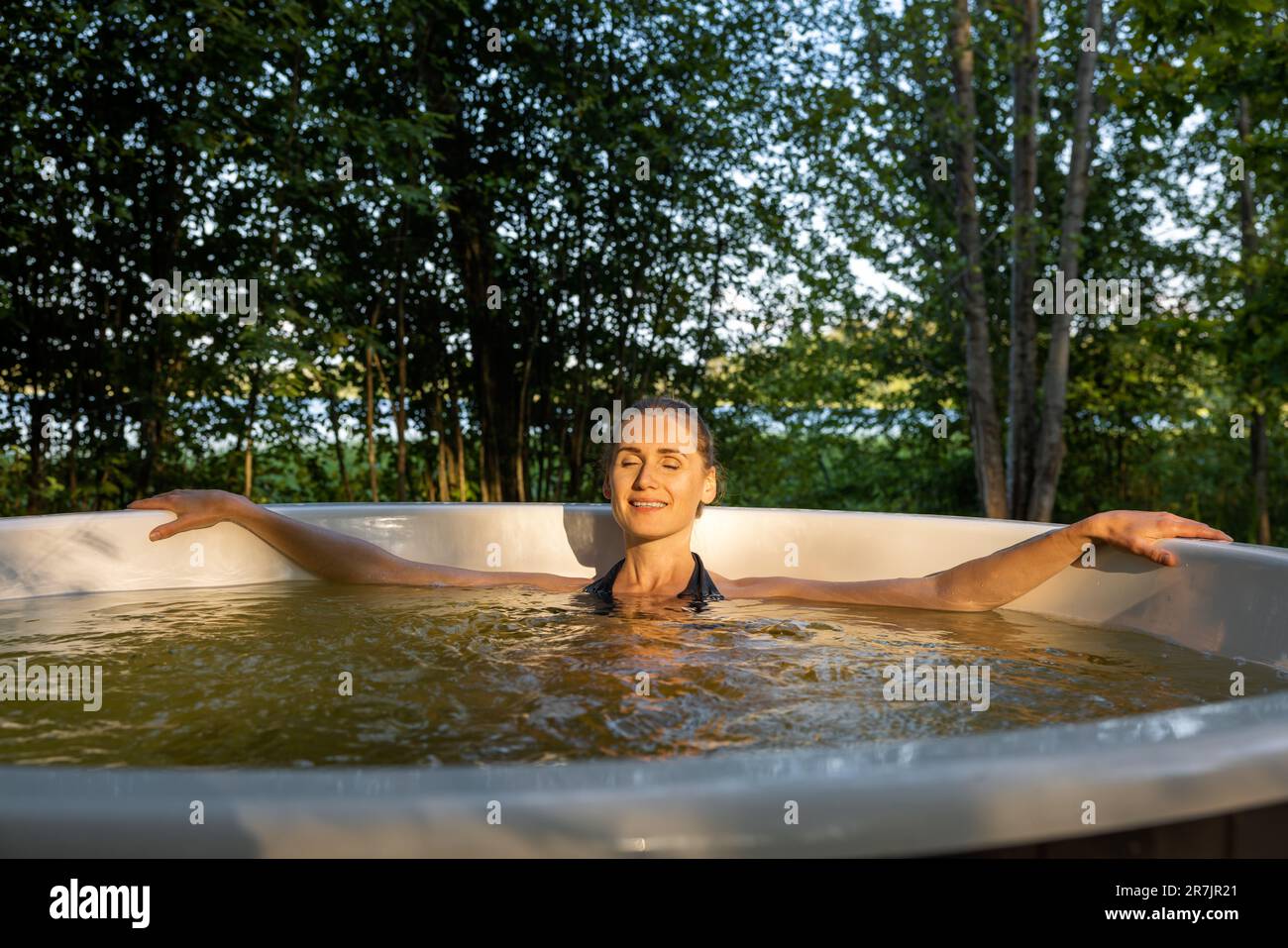 Eine Frau, die sich bei Sonnenuntergang im Wald entspannen und den Whirlpool im Freien genießen kann. Naturbad Stockfoto
