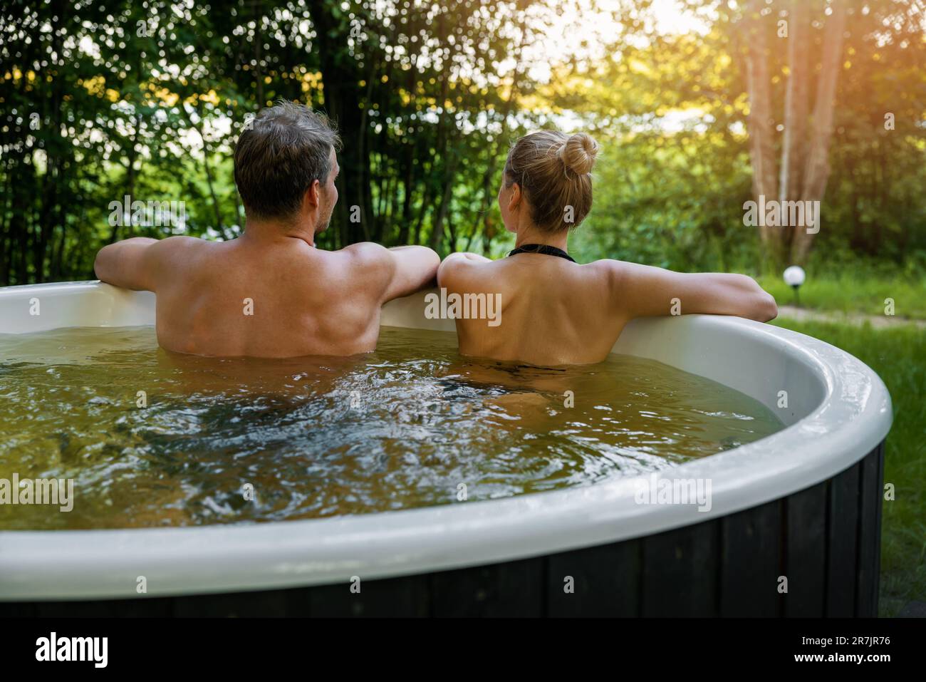 Ein junges Paar, das sich im Whirlpool im Freien im Forest Resort entspannen kann. Spa-Naturbehandlung, romantischer Kurzurlaub Stockfoto