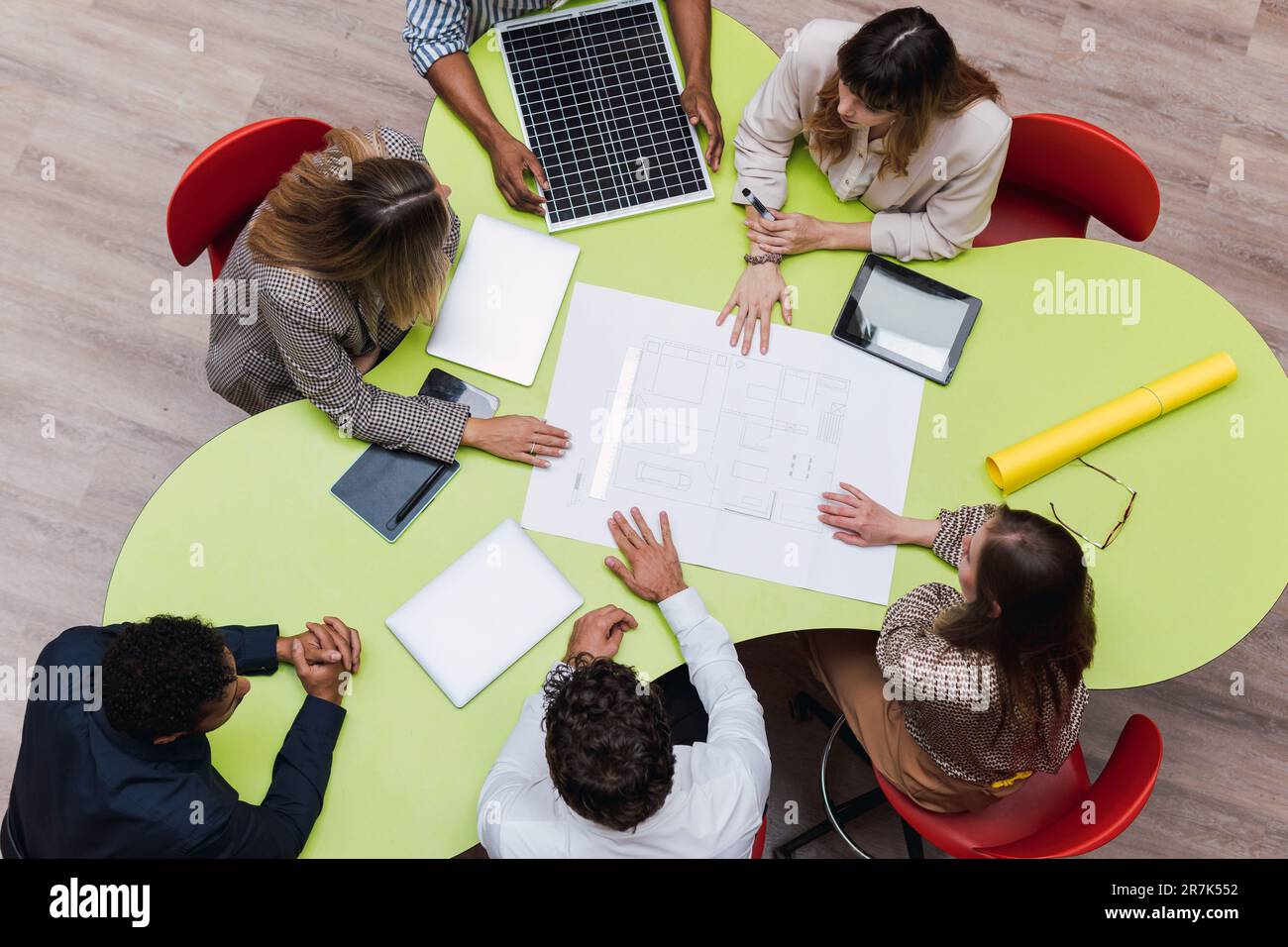 Aus einem großen Blickwinkel können Sie Kollegen sehen, die ein Meeting mit einem Plan, drahtlosen Geräten und Solarmodul auf dem Tisch abhalten Stockfoto