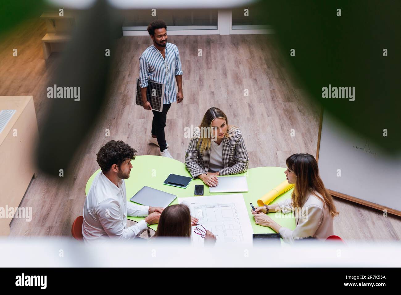 Blick aus einem großen Winkel auf Geschäftskollegen, die ein Meeting mit einem Plan und drahtlosen Geräten auf dem Tisch abhalten Stockfoto