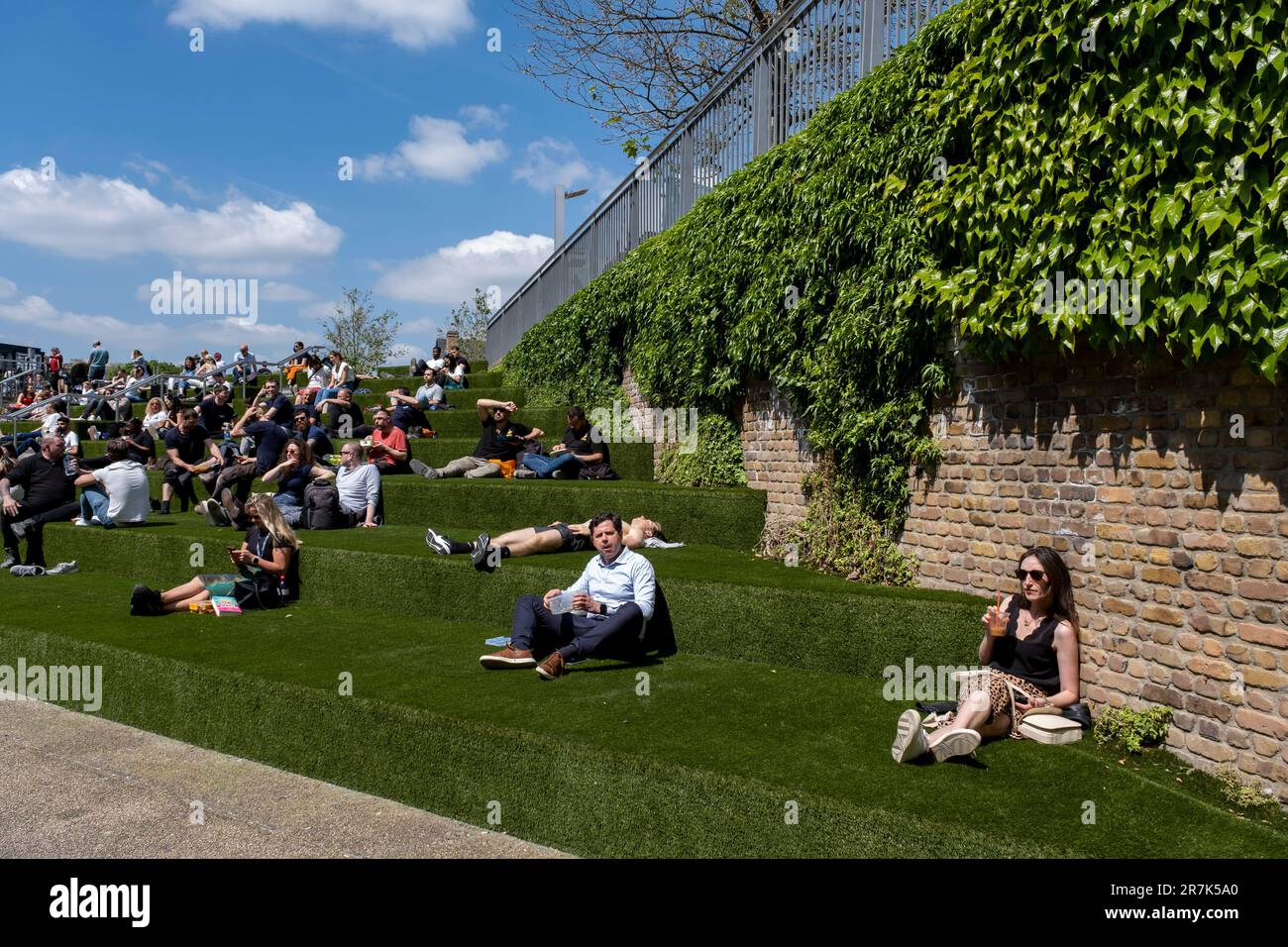 Am 24. Mai 2023 in London, Großbritannien, entspannen sich die Menschen im Frühlingssonnenschein auf den Stufen mit falschem Gras, die zum Granary Square in Kings Cross führen. Kings Cross Central ist ein Multi-Milliarden Pfund Mixed-Use-Entwicklungsgebiet auf einem Gelände, das im Besitz und unter der Kontrolle der Kings Cross Central Limited Partnership steht und etwa 67 Hektar ehemaliges Eisenbahngelände umfasst. King’s Cross ist eine der größten und transformativen Neuentwicklungen, die in London in jüngster Zeit zu sehen waren und eine ehemalige Industriestätte in ein erneuertes und lebendiges Gebiet mit Plätzen, Parks, Häusern, Geschäften, Büros, Galerien, Bars, Restaurants Stockfoto