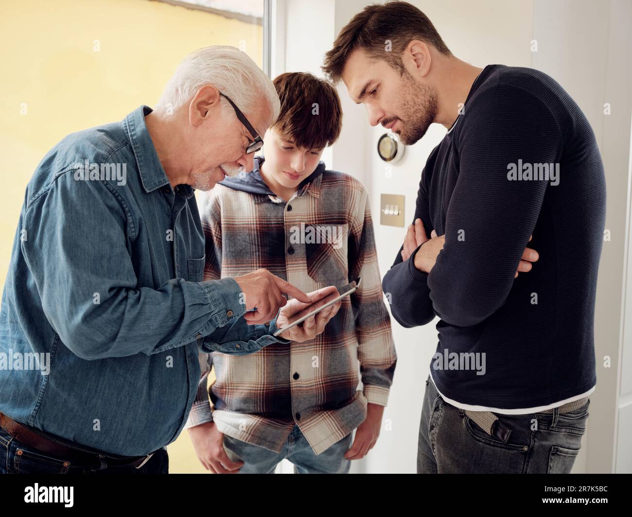 Mein Sohn, mein Vater und mein Großvater sehen sich die intelligente Thermostatsteuerung auf einem digitalen Tablet zu Hause an Stockfoto