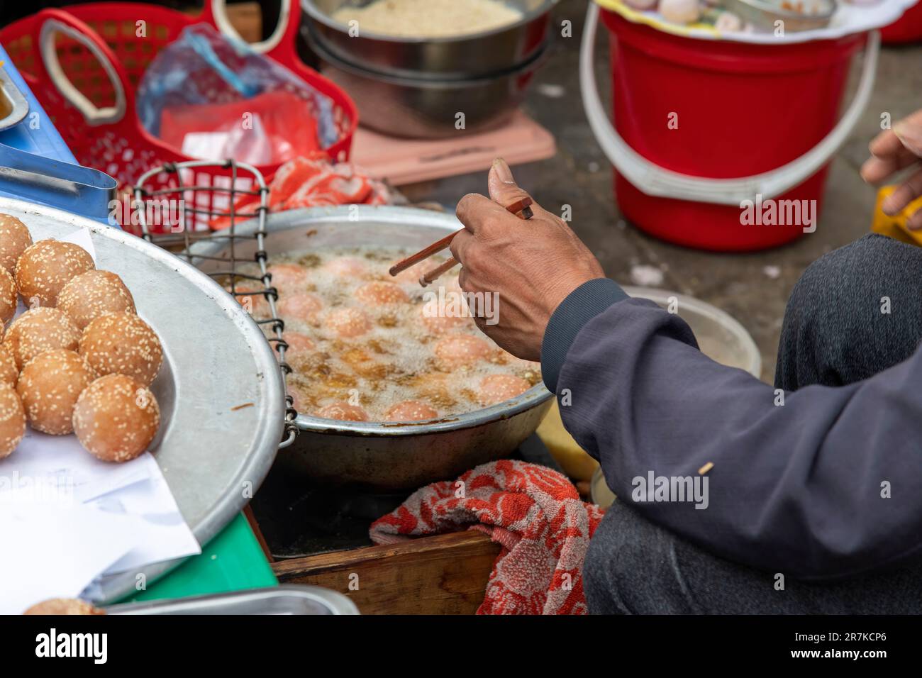 Nahaufnahme der Hand über einer Bratpfanne eines Mannes mit Stäbchen, der auf dem Bac-Ha-Sonntagsmarkt in Vietnam Doughy-Fischbällchen zubereitet Stockfoto