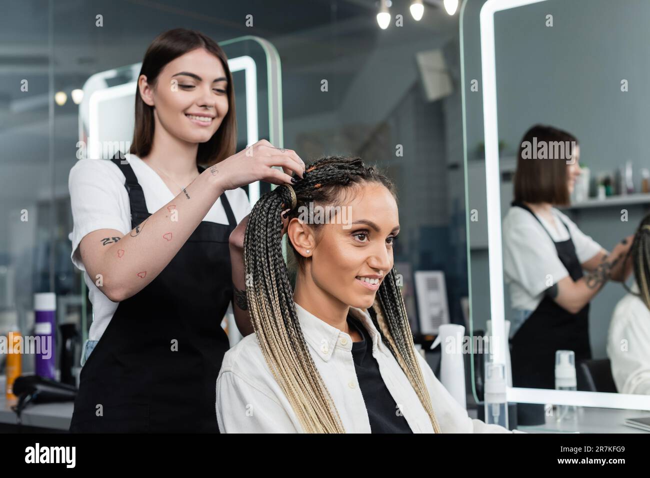 Friseur und Kundin, Schönheitssalon, tätowierte Friseurin, die einer fröhlichen Frau Haare macht, mit Zöpfen, zwei Pferdeschwanzen, Kundenzufriedenheit, Ba Stockfoto