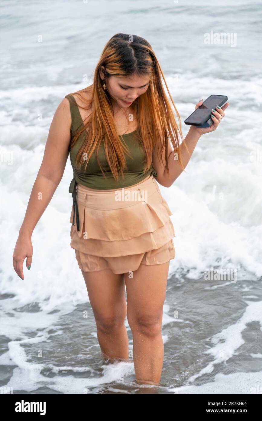 Halten Sie ihr Handy für Selfies, an einem Strand in der Nähe von Manila in der Dämmerung, schlendern Sie ziellos durch die warmen Küstengewässer, entlang des sanften Sandes, haben Sie Spaß, tanzen Sie herum Stockfoto