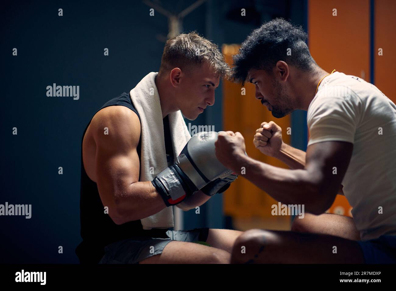 Attraktiver junger Boxspieler sitzt in der Garderobe und der Personal Trainer bereitet sich auf das Training vor. Coache den Spieler. Kampfsport, Sport, Stockfoto