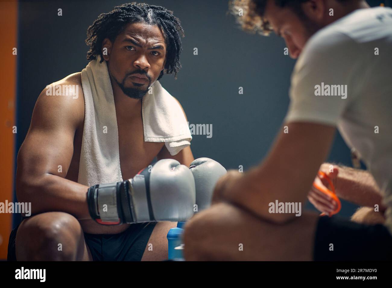 Starker, starker junger Boxspieler mit Trainer, der sich auf das Training vorbereitet und von Angesicht zu Angesicht auf der Bank sitzt. Sport, Lifestyle-Konzept. Stockfoto