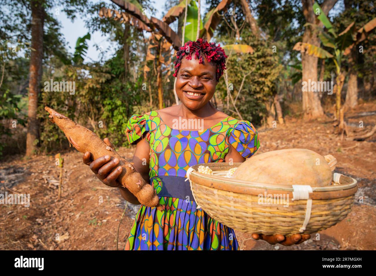 Eine lächelnde Bäuerin mit ihrem Erntekorb auf den Feldern, Kleinunternehmer in Afrika Stockfoto