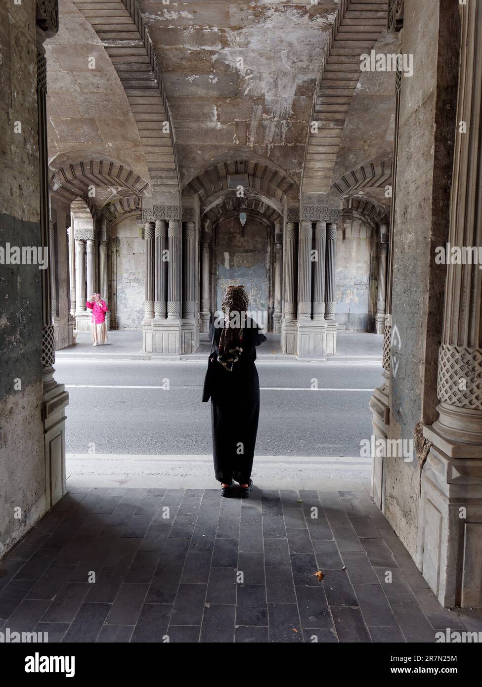 Frauen in schwarz-rosa Außenwänden mit goldenen Kopftüchern stehen unter einer eleganten Brücke neben der Straße im Stadtteil Beşiktaş in Istanbul, Türkei Stockfoto