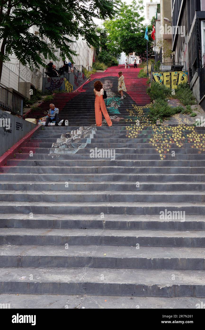 Frau in orangenem Outfit steht abends auf gemalten steilen Stufen im Stadtteil Karakoy in Istanbul, Türkei Stockfoto